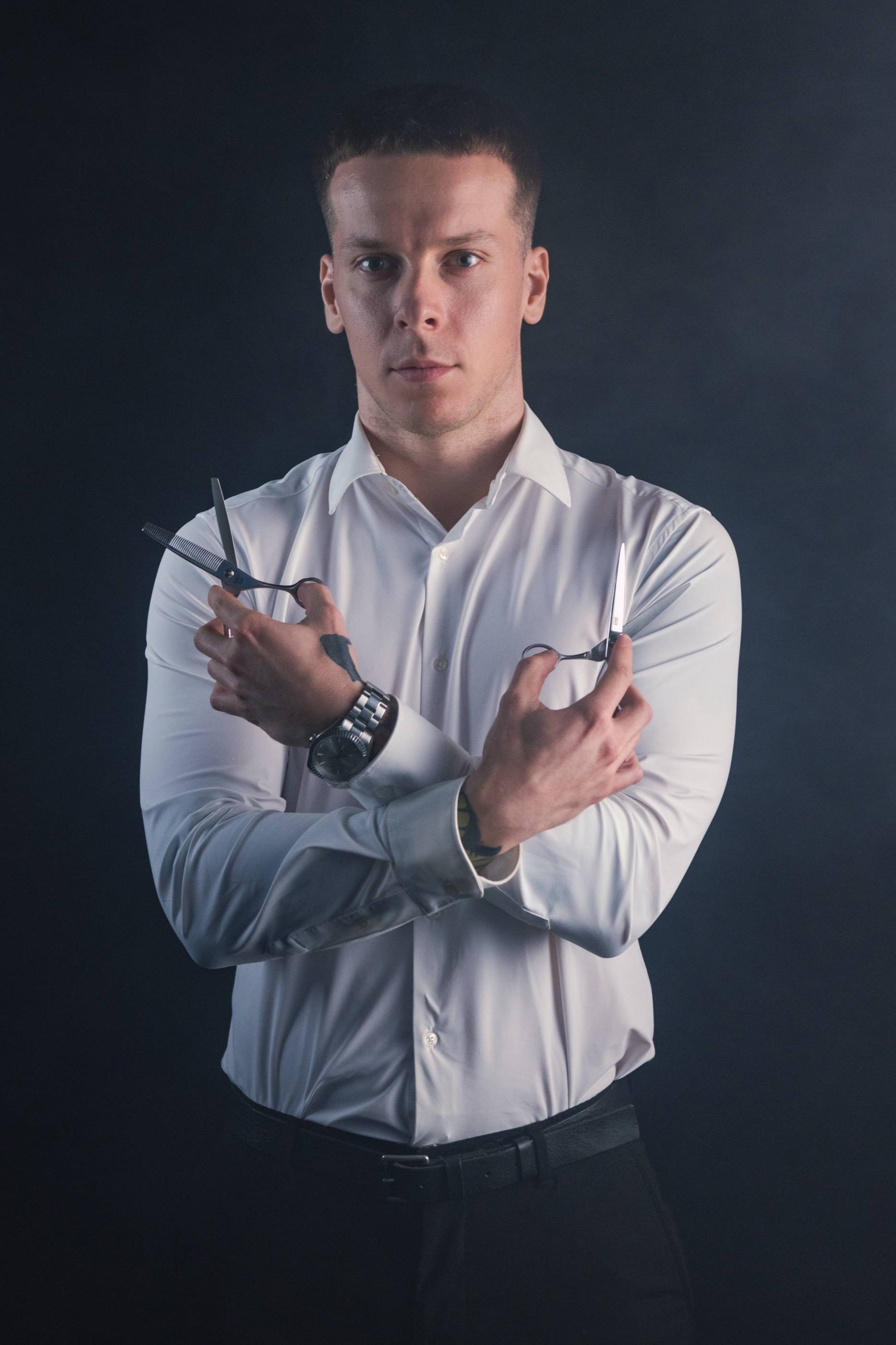 Viliam „Vilis“ Sliacky v bielej košeli, v prekrížených rukách drží nožnice